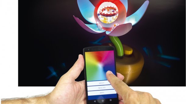 Zwei Hände halten ein Smartphone vor eine Blume aus dem 3D-Drucker