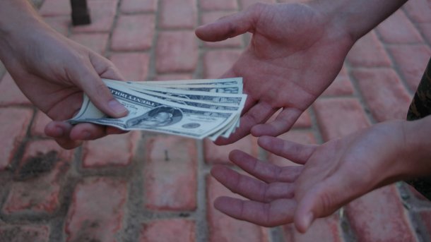 Eine Hand reicht Dollarscheine, zwei Hände empfangen sie 