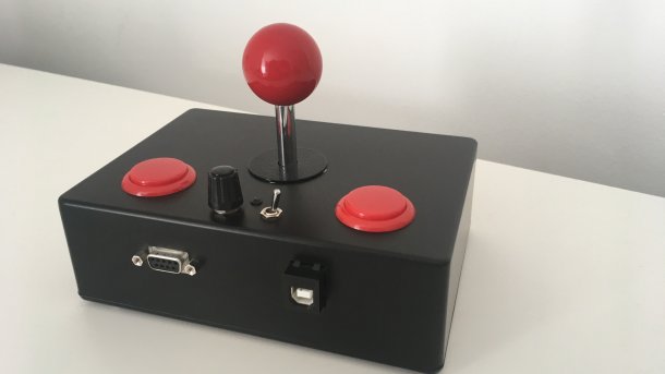 Ein schwarzes, rechteckiges Gehäuse aus Metall, aus dem zwei rote Buttons, ein Kippschalter, ein Potentiometer und ein roter Joystick ragen.