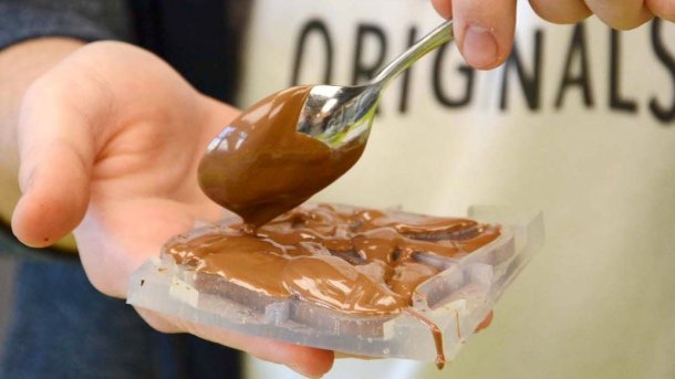 Eine Hand hält eine transparente Silikonform, in die mit einem Löffel Schokolade gefüllt wird.