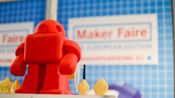 Ein roter Roboter Makey aus dem 3D-Drucker, im Hintergrund der Schriftzug "Maker Faire".