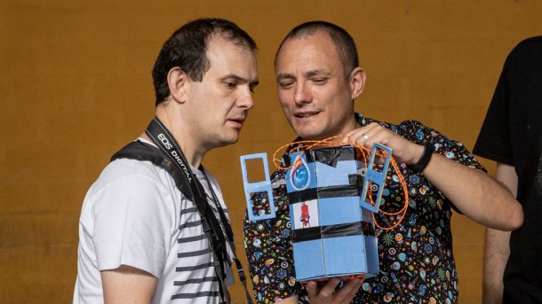 Zwei Männer schauen auf einen blauen Kasten mit zwei kleinen Antennen.