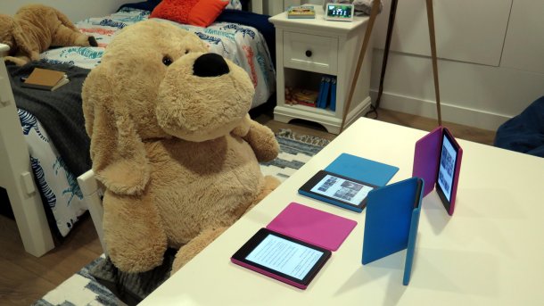 Großer Teddybär sitzt vor 4 Kindles mit bunten Hüllen