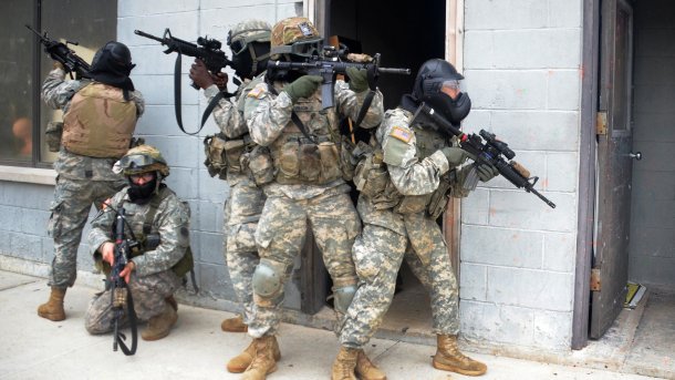 Bewaffnete Soldaten in Tarnanzügen und Atemschutz vor Gebäude