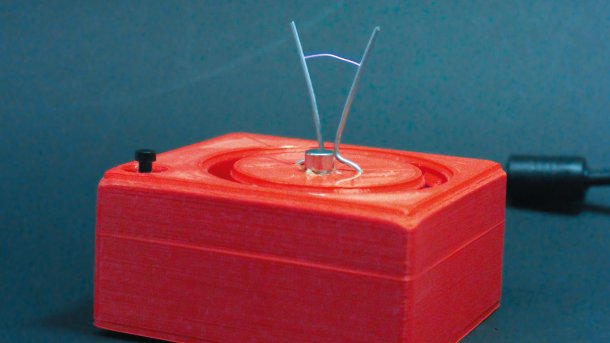 Das Jakobs-Leiterchen: eine rote Kiste aus der zwei Metallstäbe rausragen und sich voneinander entfernen. Dazwischen leuchtet ein Blitz auf.