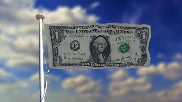 1-USD-Note wie eine Fahne auf Fahnenmast montiert, dahinter blauer Himmel mit weißen Wolken