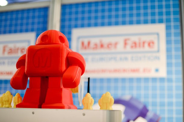 Ein roter Roboter Makey aus dem 3D-Drucker, im Hintergrund der Schriftzug "Maker Faire".