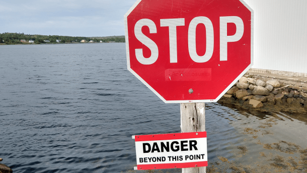 Stoptafel mit Zusatzschild "DANGER beyond this point" - dahinter Meereswasser