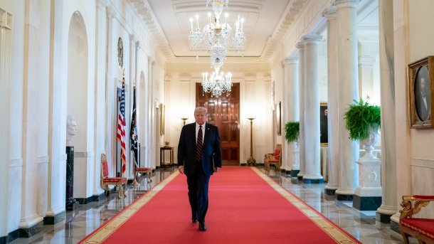 Donald Trump geht auf rotem Teppich durch weißen Gang