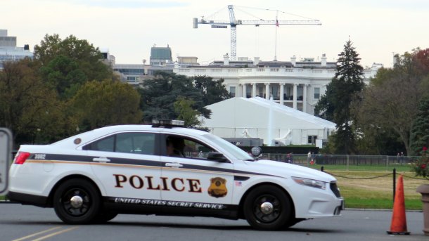 Ein Polizeiauto steht vor dem Weißen Haus, darin sitzten 2 Personen.