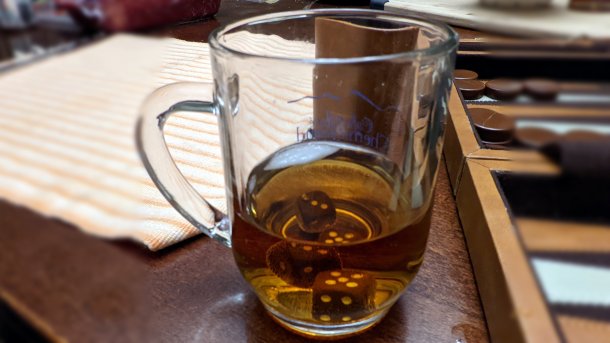 Teilweise mit Tee gefülltes Glas, darin liegen Spielwürfel