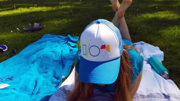 Blonde Frau liegt im Gras, trägt mit Kappe mit "I/O 19"-Logo