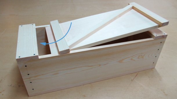 Schritt 1 beim Schließen der Kiste: Deckel schräg mit dem langen Anschlag unter das Endstück schieben.