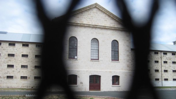 Blick durch Gitter auf ein steinernes Gefängnisgebäude