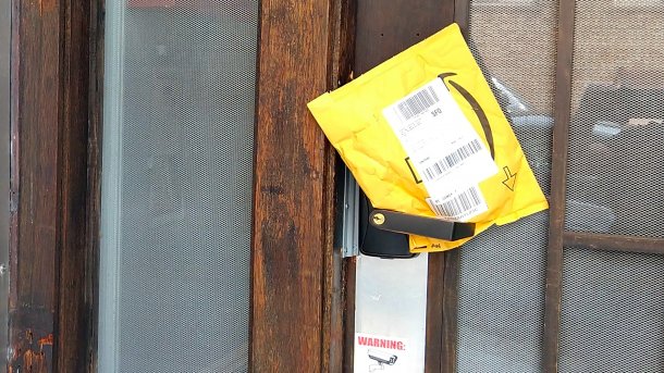 Haustüre mit Gegensprechanlage. In der Türschnalle ist ein Amazon-Kuvert eingeklemmt.