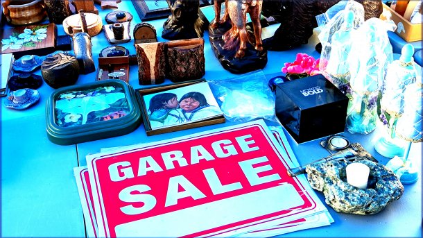 Tisch eines Flohmarkts; Tand; darunter ein Stoß Schilder "Garage Sale"