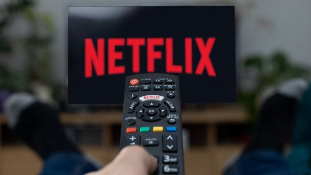 Fernbedienung in der Hand, Netflix-Logo auf Fernseher