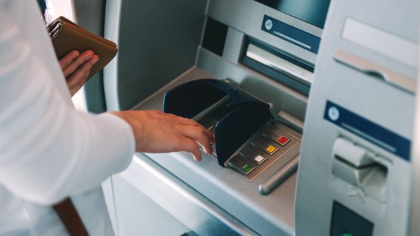 Eine Frau mit einer Geldbörse in der Hand an einem Geldautomaten.