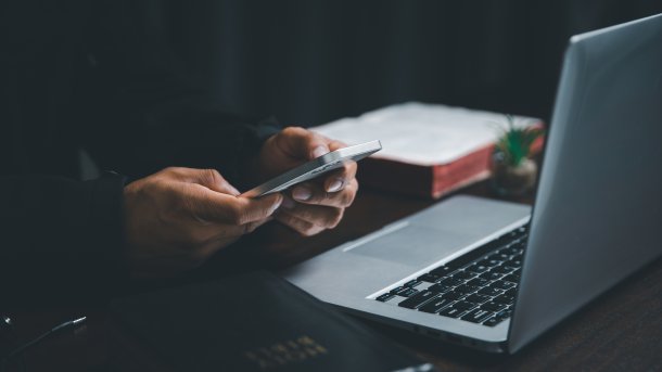 Person an Smartphone und Laptop mit mehreren Bibeln