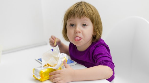 Kind isst Kekse, spielt an einem Tablet und streckt die Zunge in die Kamera