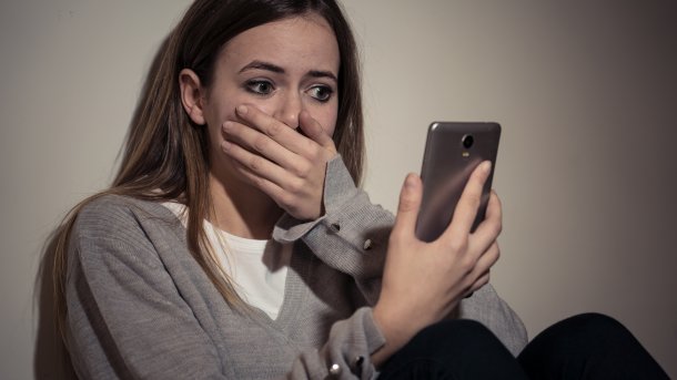 Mädchen blickt erschreckt auf ihr Smartphone