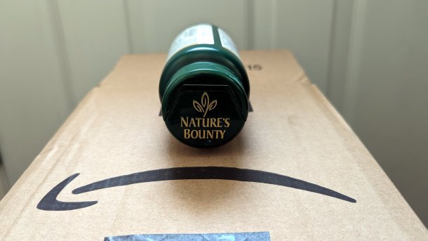Eine grüne Plastiksode mit Aufschrift "Nature's Bounty" liegt auf einer Amazon-Versandschachtel