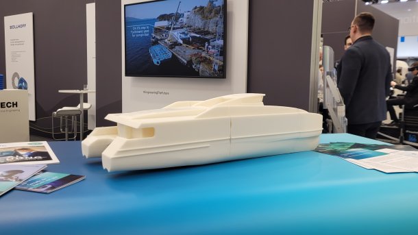 Schiffsmodell aus 3D-Druck liegt auf einem Tisch in einer Messehalle