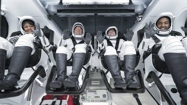 Vier Menschen in Raumanzügen in einer Raumkapsel