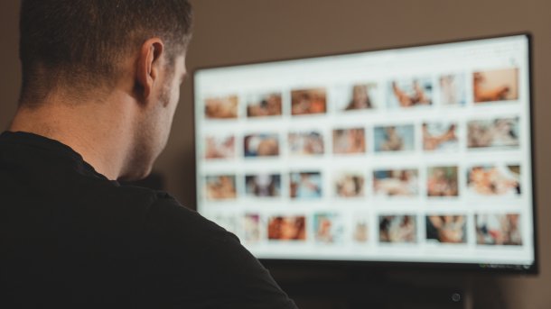 Mann schaut in einem abgedunkelten Raum pornografische Bilder auf einem Computerbildschirm an.