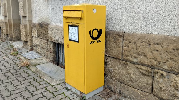 Ein gelber Briefkasten der Deutschen Post steht an einer Gebäudewand