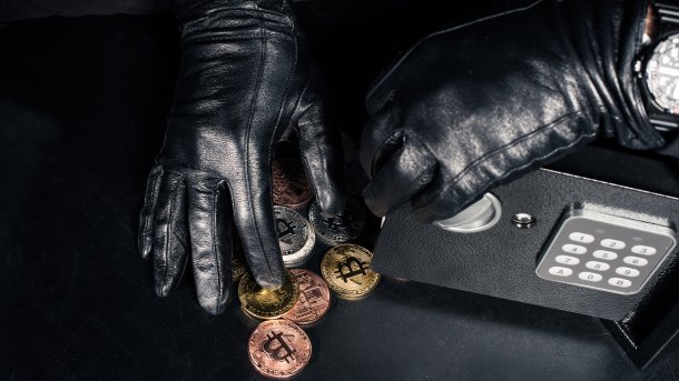 Zwei lederbehandschuhte Hände räumen Münzen mit Kryptowährungslogos in einen oder aus einem Tresor
