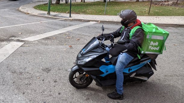 Eine Person auf einem Motoroller; hinten ein grüner Würfel mit Aufschrift "Bolt Food"
