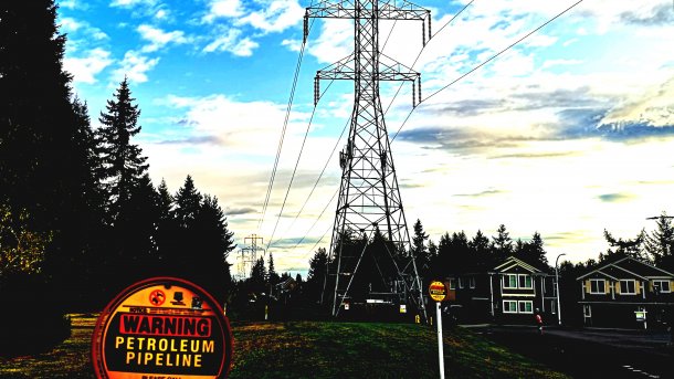 Im Hintergrund eine Hochspannungsleitung, im Vordergrund ein Schild "Warning Petroleum Pipeline"