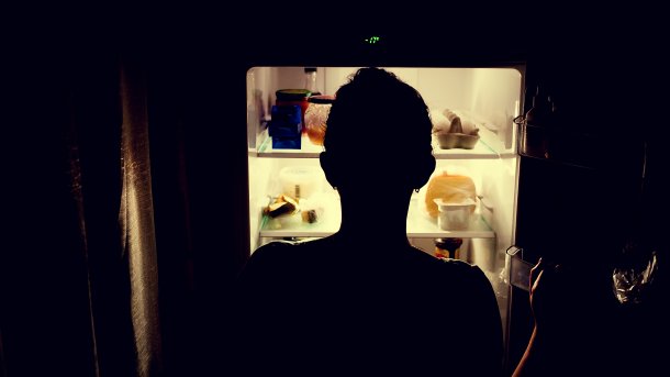 Mädchen in der Dunkelheit vor erleuchtetem Kühlschrank