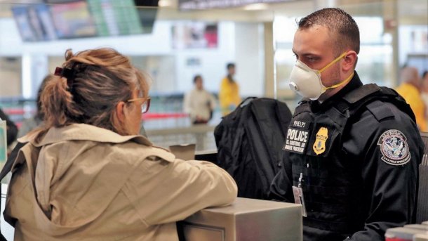Reisende mit Brille spricht mit einem unformierten Beamten der US Customs and Border Patrol auf einem Flughafen