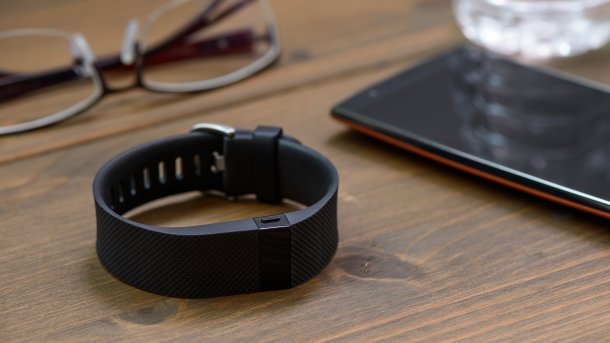 Smartes Armband, das aussieht wie ein Fitness-Tracker. Daneben liegt ein Handy neben einem Wasserglas. Dahinter befindet sich eine Brille.