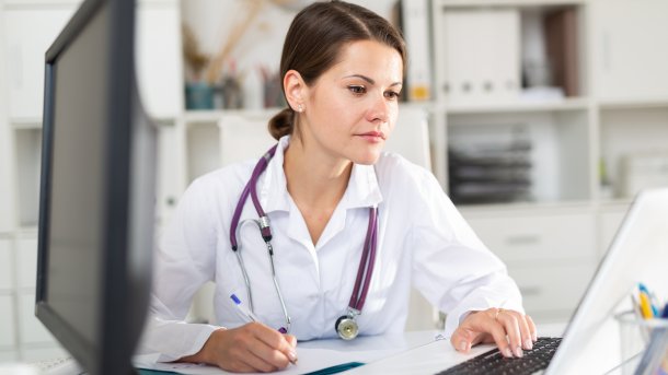 Unglücklich aussehende Ärztin vor einem Laptop, neben ihr ein zweiter Bildschirm
