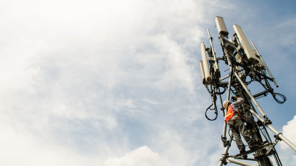 Techniker klettert an einem Antennenmast mit Mobilfunkantennen hoch.