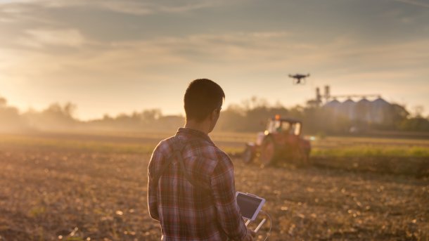 Drohne in der Landwirtschaft. Mann mit Karohemd steuert Drohne über einem Getreidefeld.