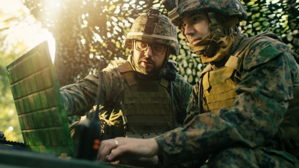 Zwei Soldaten in Tarnzeug mit Helm schauen auf einen aufgeklappten Laptop