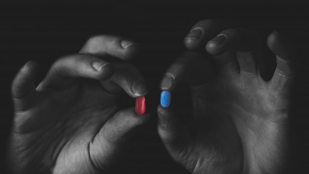 Mensch hält eine rote und eine blaue Pille in den Händen
