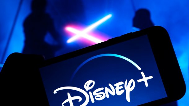 Disney+ Logo auf Mobilgerät,  im Hintergrund ein Duell mit Laserschwertern
