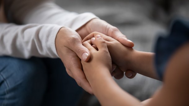 Person hält Hände von einem Kind, um es seelisch zu unterstützen