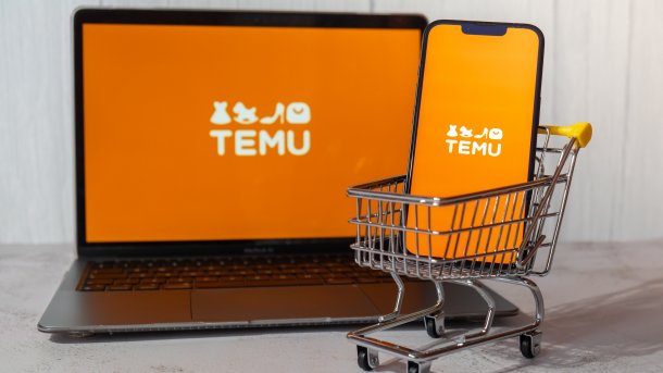 Einkaufswagen mit Temu-Website auf einem Laptop und auf dem Smartphone im Hintergrund