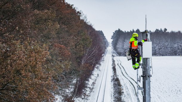 Ein Techniker an einem Funkmast im Winter, im Hintergrund die Zugstrecke