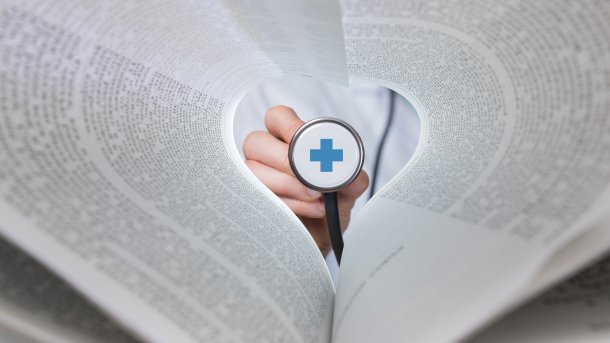 Stethoskop mit Kreuz inmitten eines Buchs mit aufgeblätterten Seiten