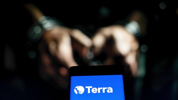 Hände in Handschellen unscharf im Hintergrund, im Vordergrund ein Smartphone mit dem Logo von Terra
