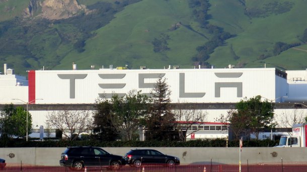 Fabrikhalle mit Aufschrift "Tesla", davor eine Autobahn