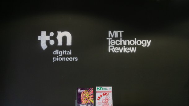 Eine schwarze Wand, auf der in weiß die Logos von t3n und MIT Technology Review in weiß abgebildet sind. Am unteren Bildrand sind die zwei Hefte aufgestellt.