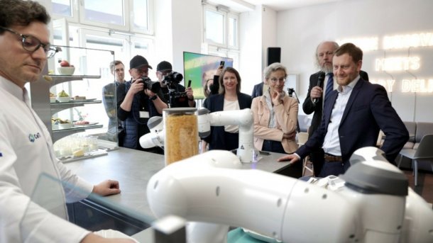 Das Bild zeigt Roboter, den Spitzenkoch Benjamin Biedlingsmaier, Ministerpräsident Sachsens Michael Kretschmer und weitere Besucher der Eröffnung der CeTIBAR.